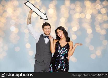 fashion, style and direction concept - happy couple with big arrow at party over festive lights background. happy couple with big arrow at party