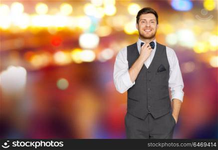 fashion, style and holidays concept - happy man in festive suit dressing for party and adjusting bowtie over night city lights background. man in festive suit over night city lights