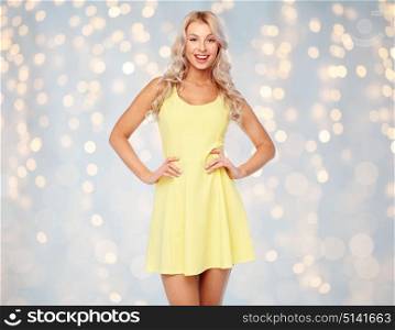 fashion, style and people concept - happy smiling beautiful young woman posing in yellow dress over holidays lights background. happy smiling beautiful young woman in dress