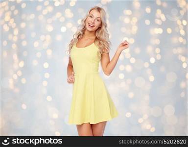 fashion, style and people concept - happy smiling beautiful young woman posing in yellow dress over holidays lights background. happy smiling beautiful young woman in dress