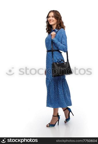 fashion, style and people concept - happy smiling beautiful young woman posing in blue dress walking over white background. happy woman in blue dress with handbag walking