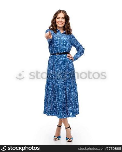 fashion, style and people concept - happy smiling beautiful young woman posing in blue dress pointing to camera over white background. happy young woman in blue dress pointing to camera