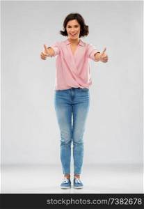 fashion, style and people concept - happy smiling young woman in striped shirt, jeans and sneakers showing thumbs up over grey background. young woman in shirt and jeans showing thumbs up