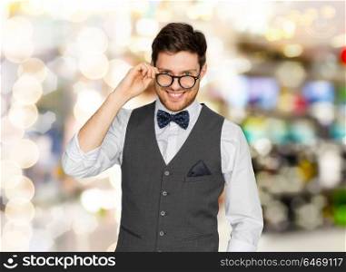 fashion, style and vintage concept - happy man in festive suit and eyeglasses over holidays lights background. happy man in suit and eyeglasses over lights