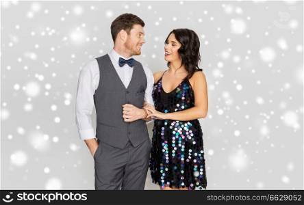 fashion, style and winter holidays concept - happy couple in festive clothes talking over grey background and snow. happy couple in festive clothes talking