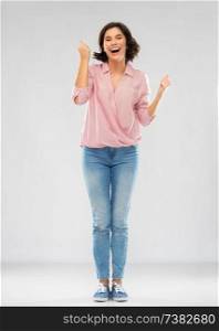 fashion, success and people concept - happy smiling young woman in striped shirt, jeans and sneakers celebrating triumph over grey background. young woman in shirt and jeans celebrating success