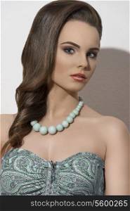 fashion summer shoot of cute brunette girl posing with smooth hair-style, make-up and green necklace
