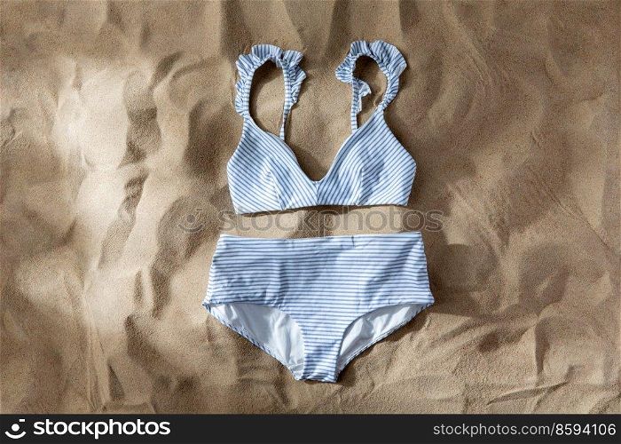 fashion, swimwear and summer holidays concept - striped white blue swimsuit top and bottom on beach sand. striped white blue swimsuit on beach sand