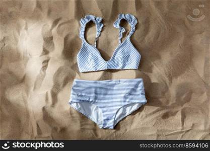 fashion, swimwear and summer holidays concept - striped white blue swimsuit top and bottom on beach sand. striped white blue swimsuit on beach sand