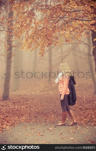 Fashion woman in foggy fall autumn park. Attractive full length young girl holding jacket. Happiness and relax in forest.