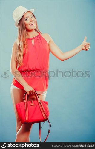 Fashion woman in hat and red shirt with handbag.. Cute attractive young woman girl in red shirt and straw hat with handbag in studio on blue showing thumb up gesture. Summer female fashion vogue.
