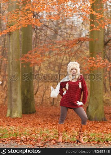 Fashion woman in windy fall autumn park forest.. Joyful fashion woman with flying scarf in windy fall autumn park forest against blowing wind. Young girl in fur cap and sweater having fun outdoor.