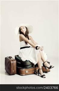 Fashion woman sitting over her luggage and waiting, isolated on a grey background