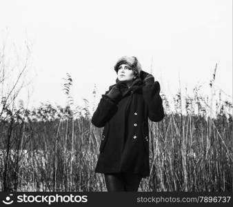 Fashion woman wearing a winter coat and fur cap and she posing front of the reeds, cold rainy weather, waist up, black and white image