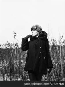 Fashion woman wearing a winter coat and fur cap and she posing front of the reeds, cold rainy weather, waist up, black and white image