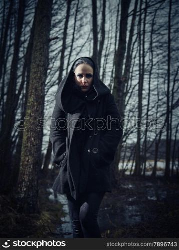Fashion woman wearing a winter coat and she pose in a gloomy forest, cold rainy weather, cross processed full length image