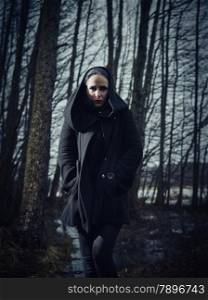 Fashion woman wearing a winter coat and she pose in a gloomy forest, cold rainy weather, cross processed full length image