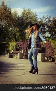 Fashion woman with bag outside. Beauty fashionable young woman having fun in park. Model wearing modern clothes in motion playing with her black bag outdoor.