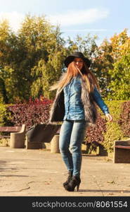 Fashion woman with bag outside. Beauty fashionable young woman having fun in park. Model wearing modern clothes in motion playing with her black bag outdoor.