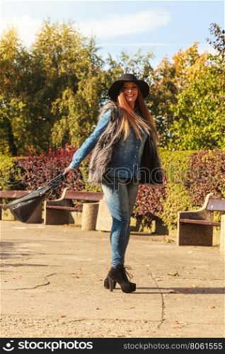 Fashion woman with bag outside. Beauty fashionable young woman having fun in park. Model wearing modern clothes in motion playing with her black bag outdoor.