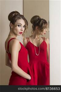 fashion woman with hairdo and make-up trying red dress in front or the mirror. Changing room. Shopping time