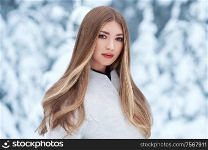 Fashion young woman in the winter forest. Young elegant model in trendy white coat in nature. Blonde girl with long smooth hair
