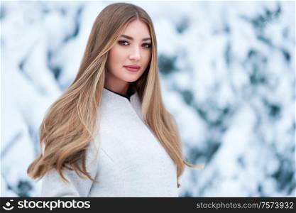 Fashion young woman in the winter forest. Young elegant model in trendy white coat in nature. Blonde girl with long smooth hair