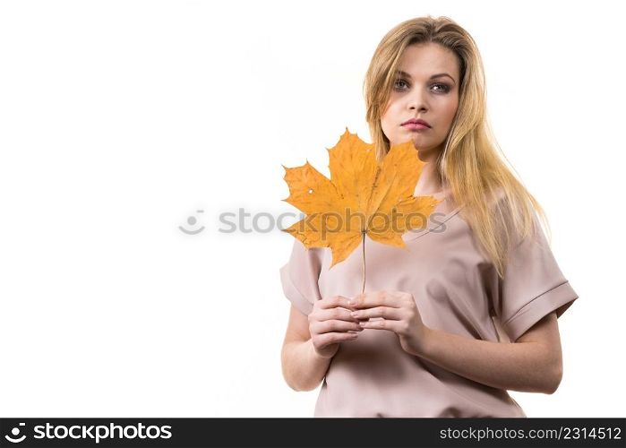 Fashionable autumn long hair blonde girl holding autumnal dry maple leaf in hand. Autumn, season and forecasting concept.. Woman holding maple leaf in hand
