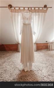 Fashionable beautiful classic lace silk wedding dress hanging on hanger in hotel wooden room. morning preparation wedding concept. vintage wedding gown.. stylish and beautiful wedding dress. classic lace silk wedding dress hanging on hanger in hotel wooden room. morning preparation wedding concept.