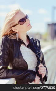 Fashionable beautiful young blond wearing a leather jacket, warm sunny day