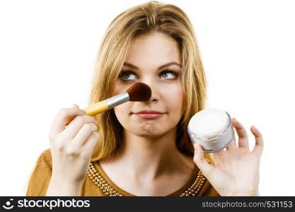 Fashionable cheerful young female holding professional powder brush, adding last touch to her make up. Smiling woman holding make up brush