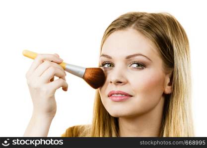 Fashionable cheerful young female holding professional powder brush, adding last touch to her make up. Woman holding make up brush