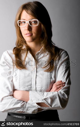 fashionable confident business woman wearing white glasses is standing with folded hands on gray background