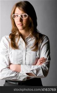 fashionable confident business woman wearing white glasses is standing with folded hands on gray background