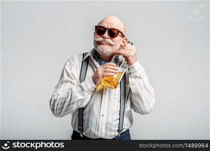 Fashionable elderly man hugs the bottle of good alcohol, grey background. Mature senior looking at camera in studio, dude. Elderly man hugs the bottle of good alcohol
