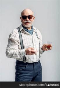 Fashionable elderly man with cigar and bottle of good alcohol, grey background. Mature senior looking at camera in studio, dude. Elderly man with cigar and bottle of good alcohol