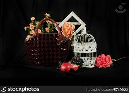 Fashionable handbag with cage fruits and flowers on black background. . Fashionable handbag composition
