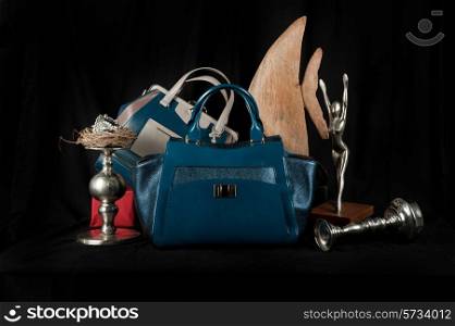 Fashionable handbag with jewelry and different items for composition on black background.