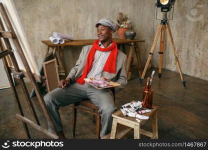 Fashionable male painter in hat and red scarf, art studio. Artist draws at his workplace, creative master works in workshop. Fashionable male painter in hat and red scarf