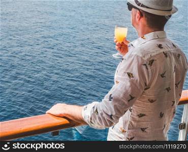 Fashionable man holding a beautiful glass of pink wine on the open deck of a cruise liner against the backdrop of blue sea waves. Side view, close-up. Concept of leisure and travel. Man holding a beautiful glass of pink wine