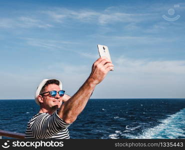 Fashionable man holding a mobile phone on the empty deck of a cruise liner against the backdrop of the sea waves. Side view, close-up. Concept of technology, recreation and travel. Fashionable man holding a mobile phone on the deck