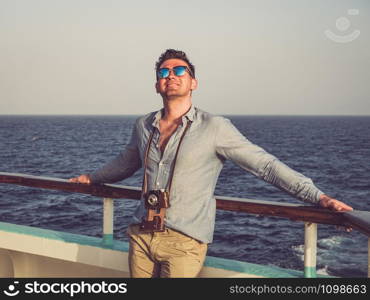 Fashionable man holding a vintage camera on the empty deck of a cruise liner against a background of sea waves. Side view, close-up. Concept of leisure and travel. Man on the empty deck of a cruise liner