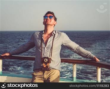 Fashionable man holding a vintage camera on the empty deck of a cruise liner against a background of sea waves. Side view, close-up. Concept of leisure and travel. Man on the empty deck of a cruise liner
