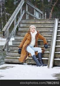 Fashionable mature adult woman wearing winter clothes and she sitting on the stairs - rural scene