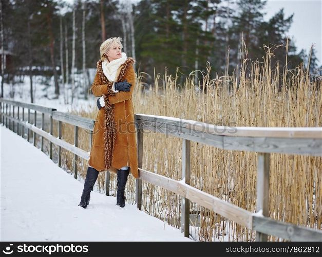 Fashionable mature adult woman wearing winter clothes and she standing next to the fence - rural scene