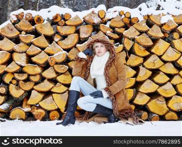 Fashionable mature adult woman wearing winter clothes, rural scene, firewood stack on background