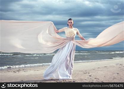 Fashionable model holding a flying long dress. Exclusive dress. Blue sky background