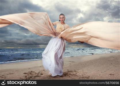 Fashionable model posing in extremely long dress on the seashore