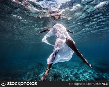 Fashionable model wearing white long dress dive into the water, dancing underwater, summer vacation, sport and art concept