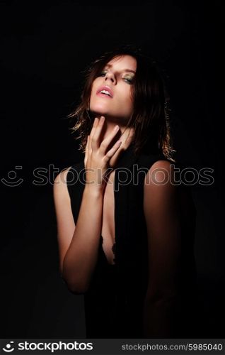 Fashionable portrait of a young woman, posing on a dark background, in the studio, hand near chin.